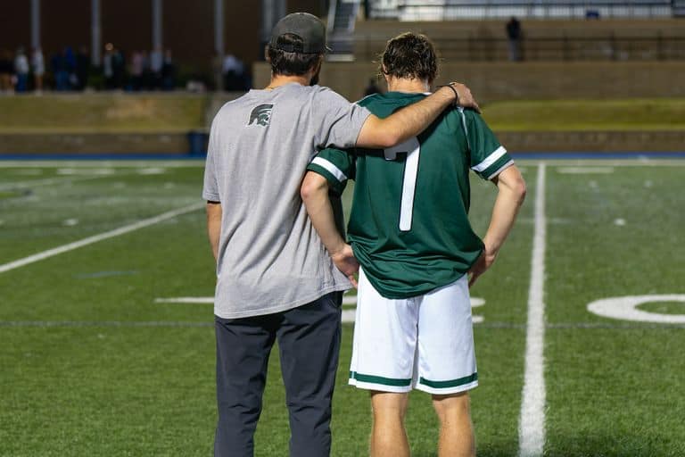 A coach embraces and supports a soccer player on the field, fostering teamwork.